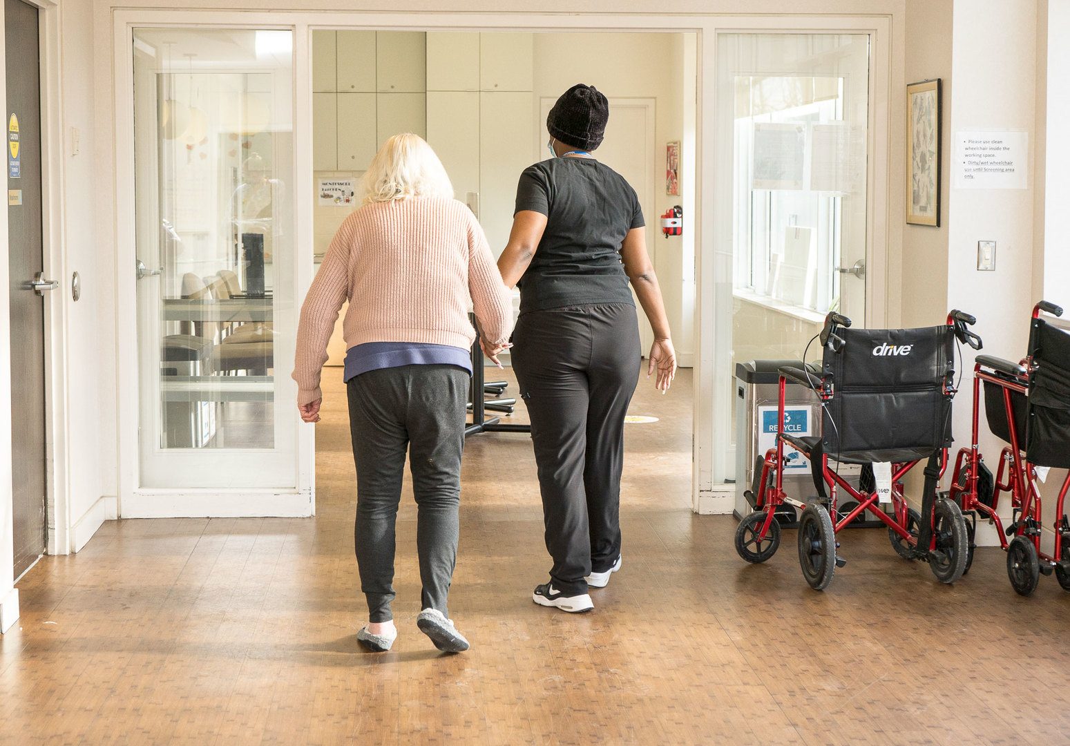 Senior and a Personal Support Working walking hand in hand down a hallway