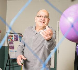 A Lumacare senior man smiling as he plays with a ball
