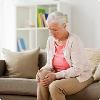 Older adult holding a sore knee while sat on a couch