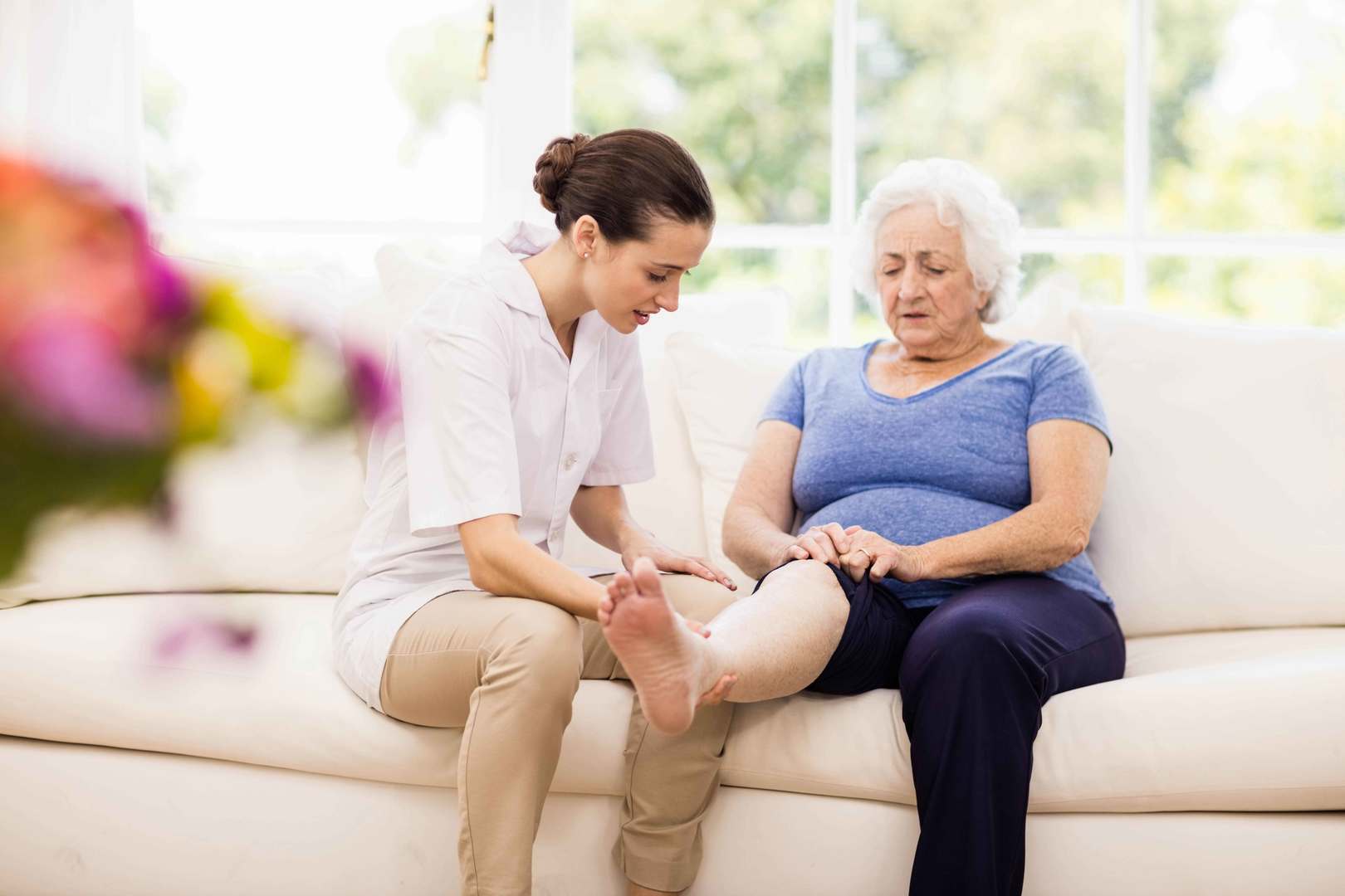 A chiropodic nurse cares for a senior seated on a couch