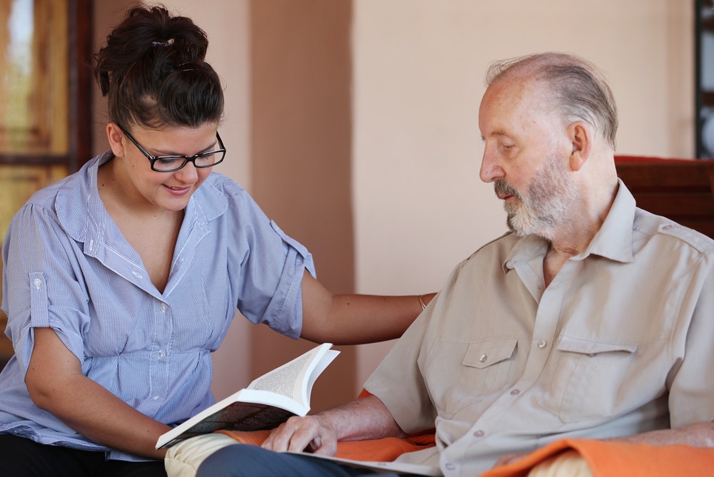 A Personal Support Worker student reads to a senior man in a chair